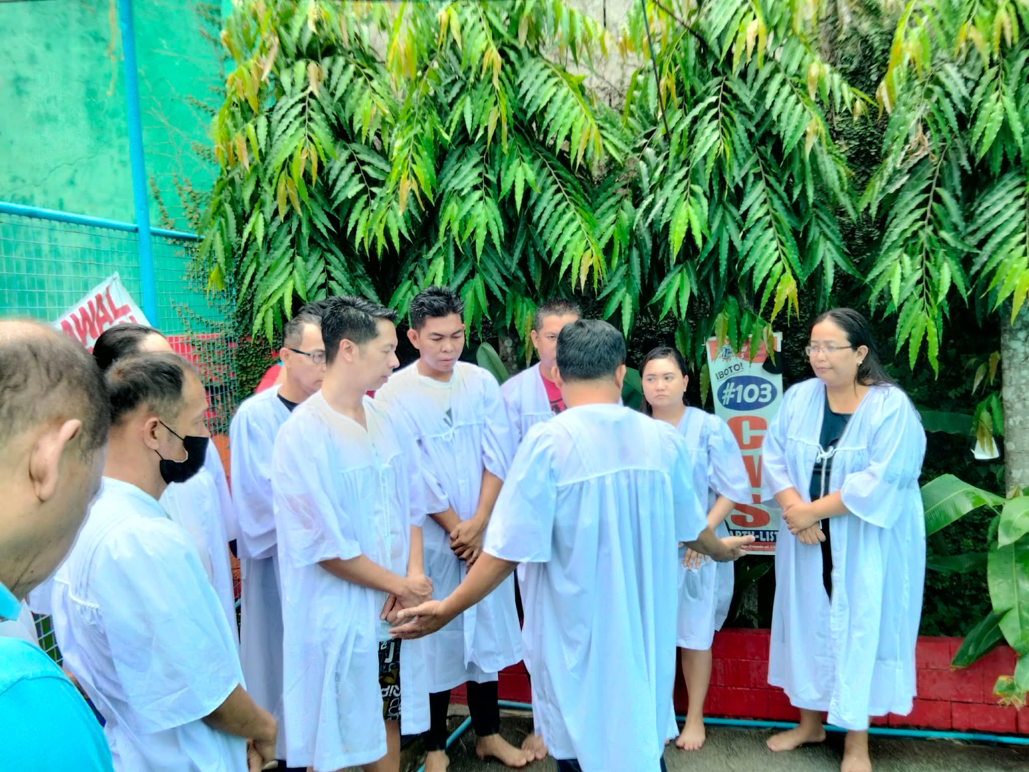 Prayer before baptism at an outdoor pool surrounded by greenery