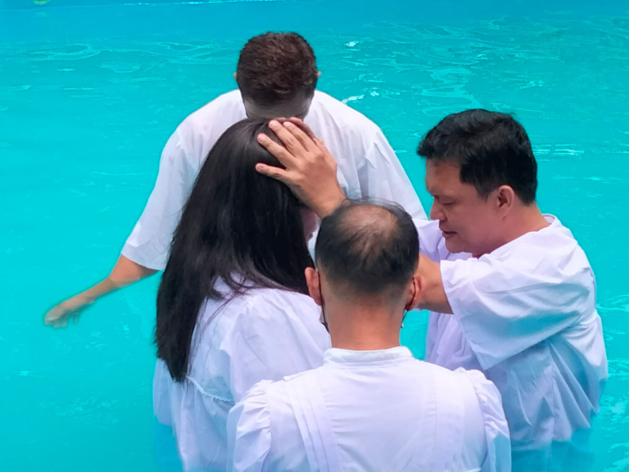 Candidate being baptized by immersion in the pool while ministers assist