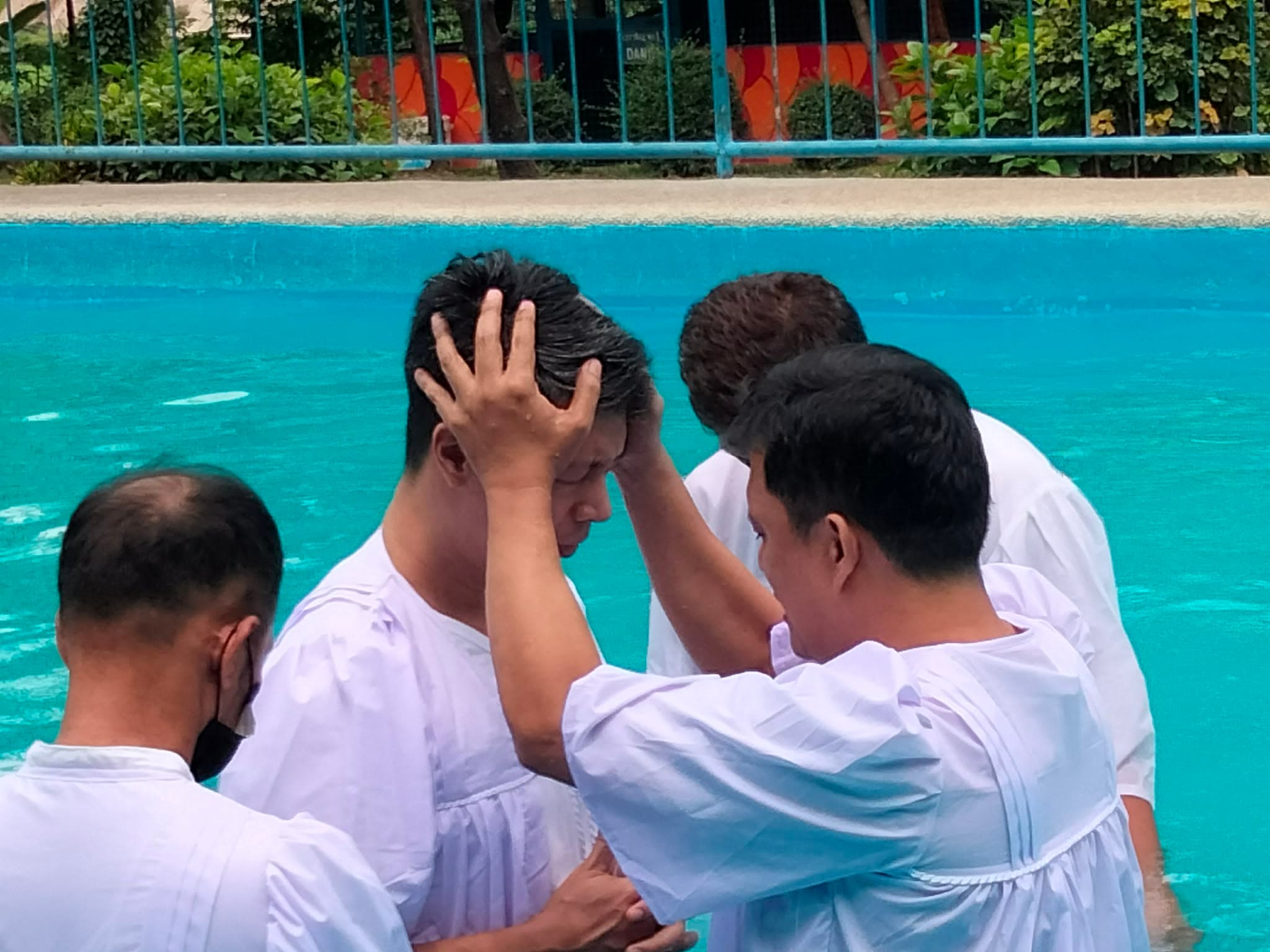 Ministers supporting a candidate during baptism in the clear pool water